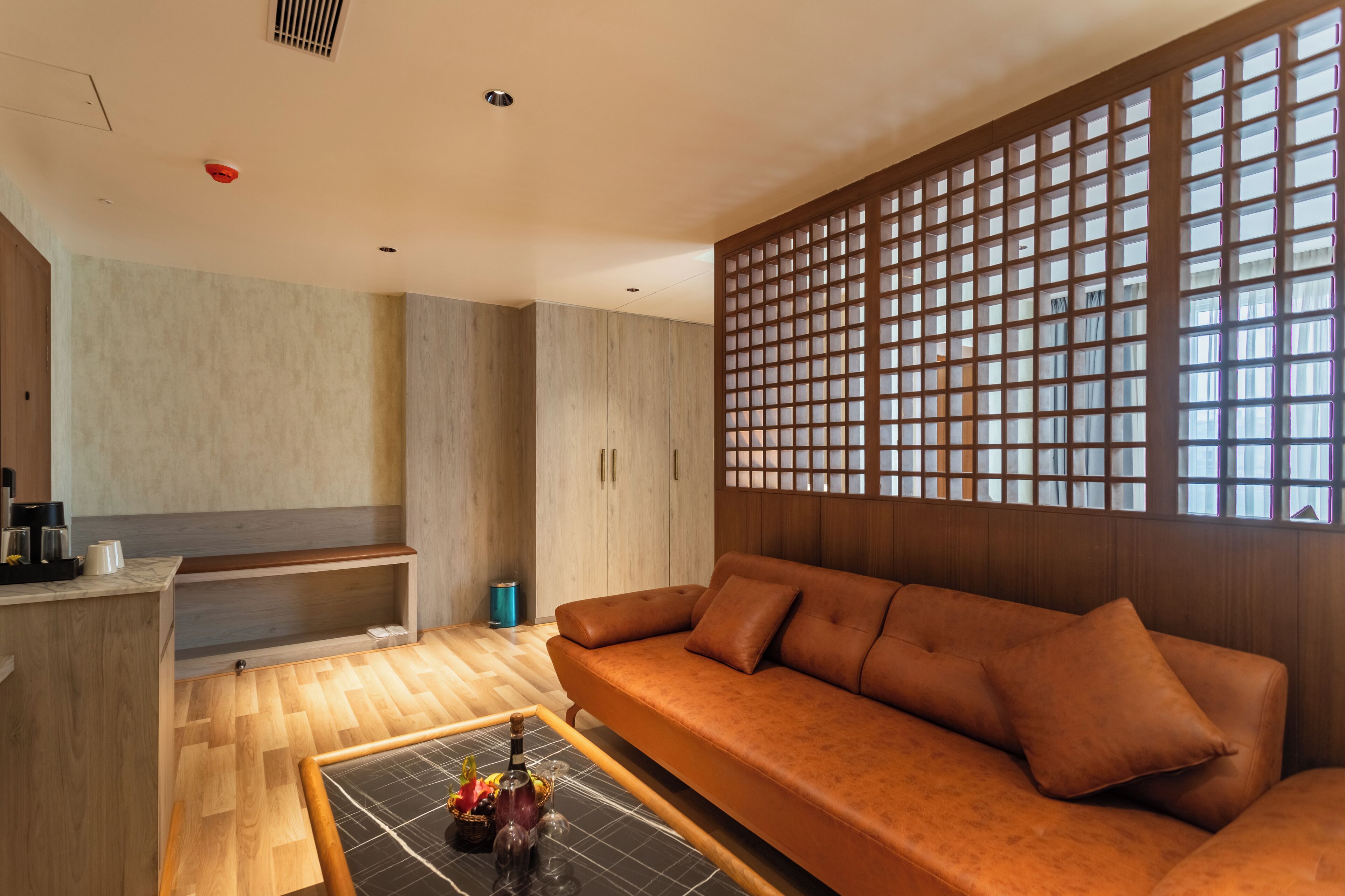 A modern room with a wooden sofa, a small table with a bottle and glasses, and a partition with a grid pattern.