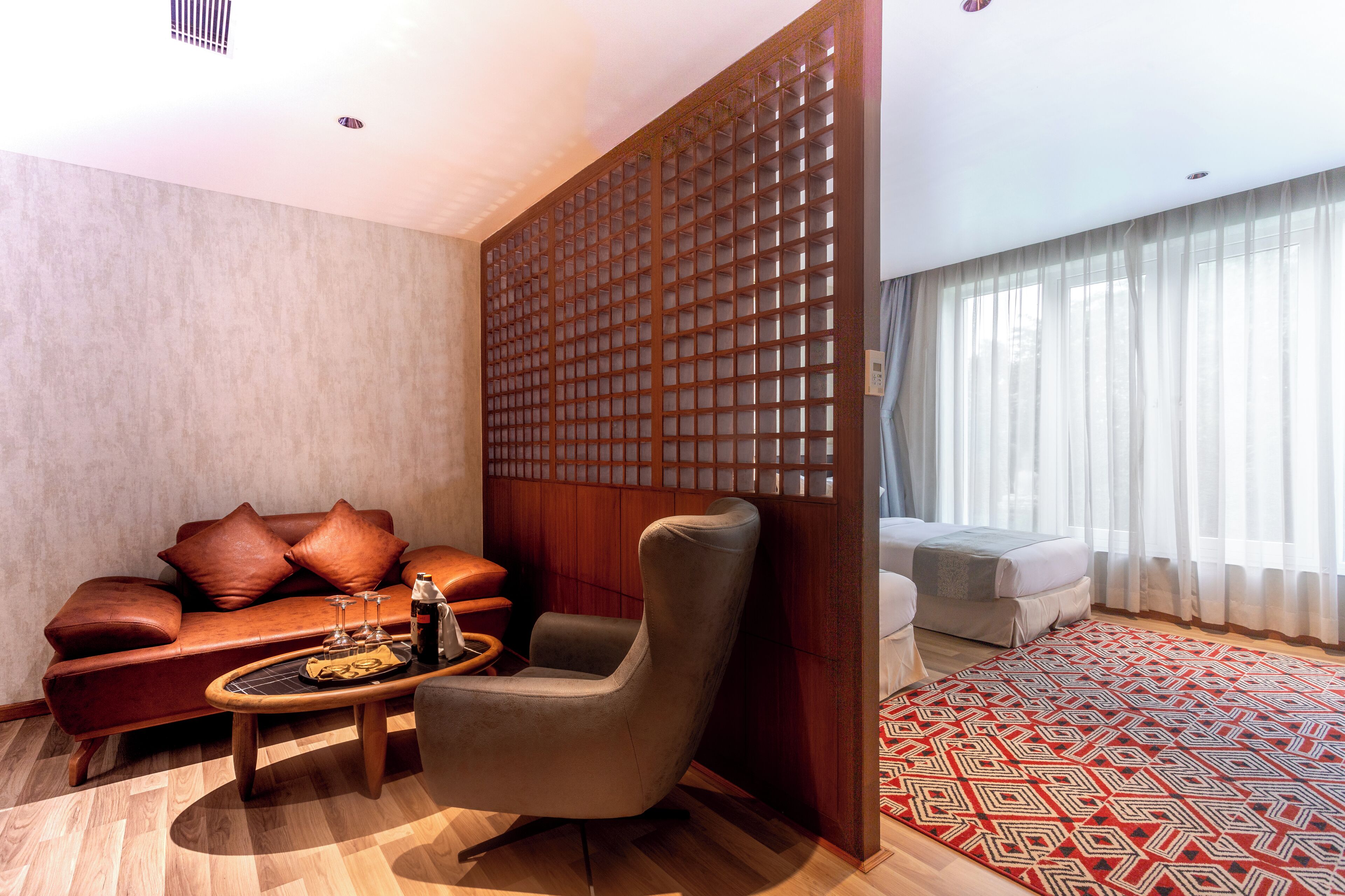 A modern living room with a leather sofa, a wooden partition, and a patterned rug.
