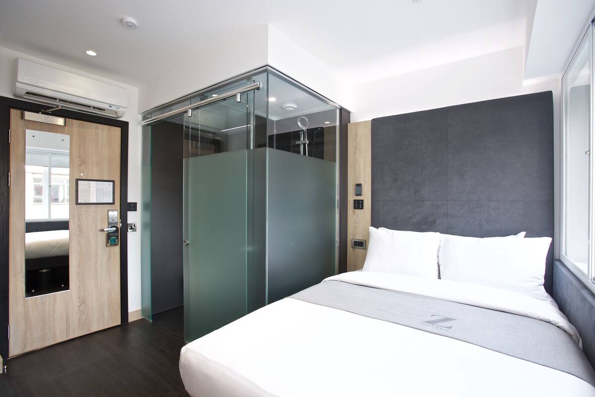 Una habitación de hotel moderna con cama, ducha de vidrio y puerta de madera.