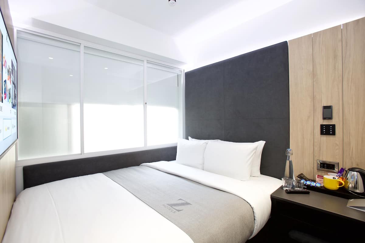 Una habitación de hotel moderna con cama, mesita de noche y un amplio ventanal.