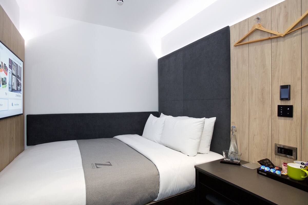 Una habitación de hotel moderna con una cama grande, una mesita de noche con cafetera y un televisor en la pared.