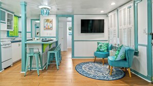 Une cuisine avec un coin repas, un téléviseur fixé au mur et un canapé de couleur turquoise assorti de coussins.