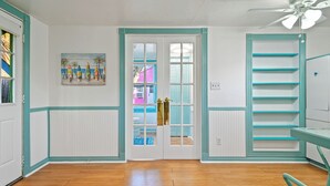 Une pièce avec un plancher en bois, une porte à panneaux de verre, un ventilateur de plafond et une étagère.