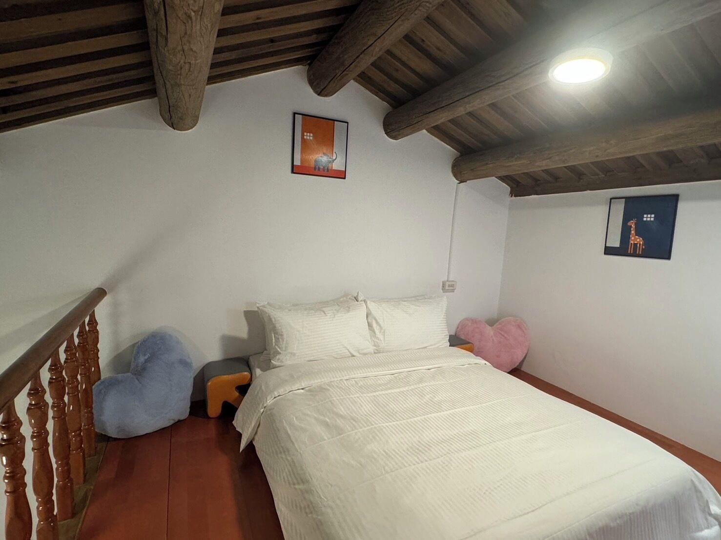 A bedroom with a wooden ceiling, a bed with white bedding, a small stool, and two wall-mounted pictures.