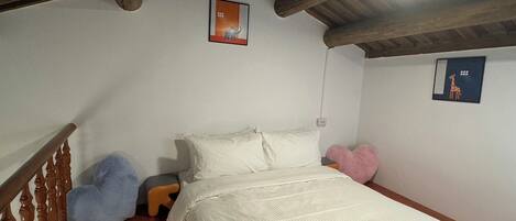 A bedroom with a wooden ceiling, a bed with white bedding, a small stool, and two wall-mounted pictures.