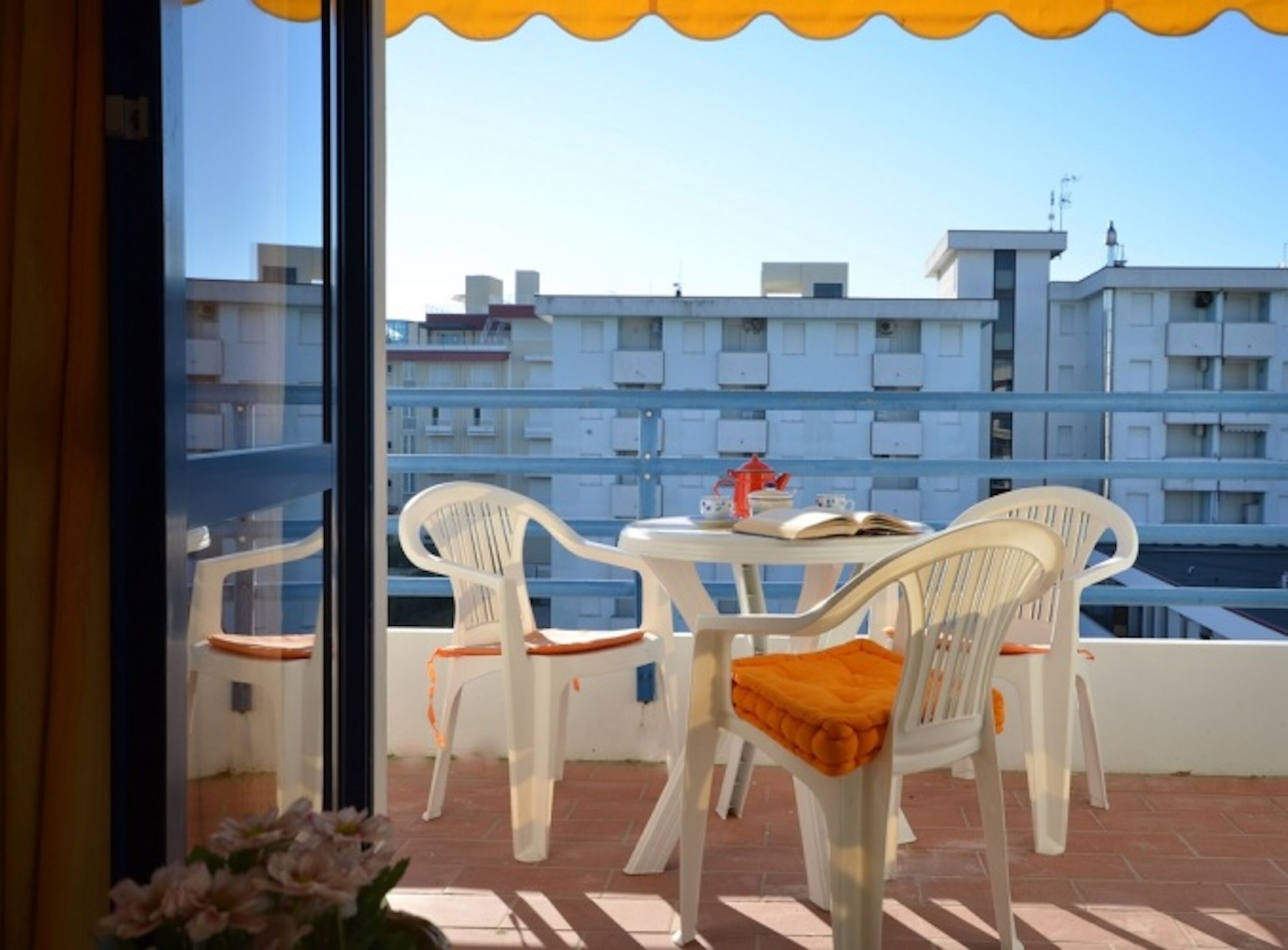 A balcony with white plastic chairs and a table, overlooking a residential area with multiple buildings.