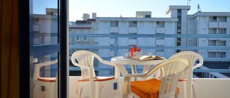 Un balcón con sillas y una mesa de plástico blanco, con vista a una zona residencial con varios edificios.