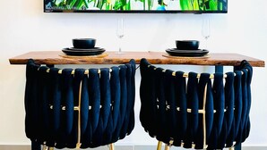Un coin repas avec une table en bois et deux chaises en velours noir aux pieds dorés. Un téléviseur à écran plat fixé au mur diffuse une scène de la nature.