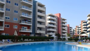 Un immeuble d’appartements moderne doté d’une piscine, de nombreux balcons et d’espaces extérieurs aménagés pour se détendre.