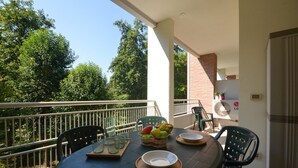 Een balkon met een ronde tafel, stoelen, een fruitmand en een ventilator.