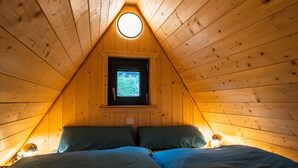 A cozy attic bedroom with a sloped ceiling, a small window, and a bed with two pillows. - Taunus Tinyhouse (Weilrod)