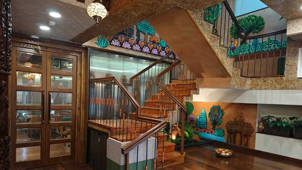 A multi-level wooden staircase with a green and brown color scheme, surrounded by decorative wall art and a small table with a candle. - Atithyaa (Bengaluru)