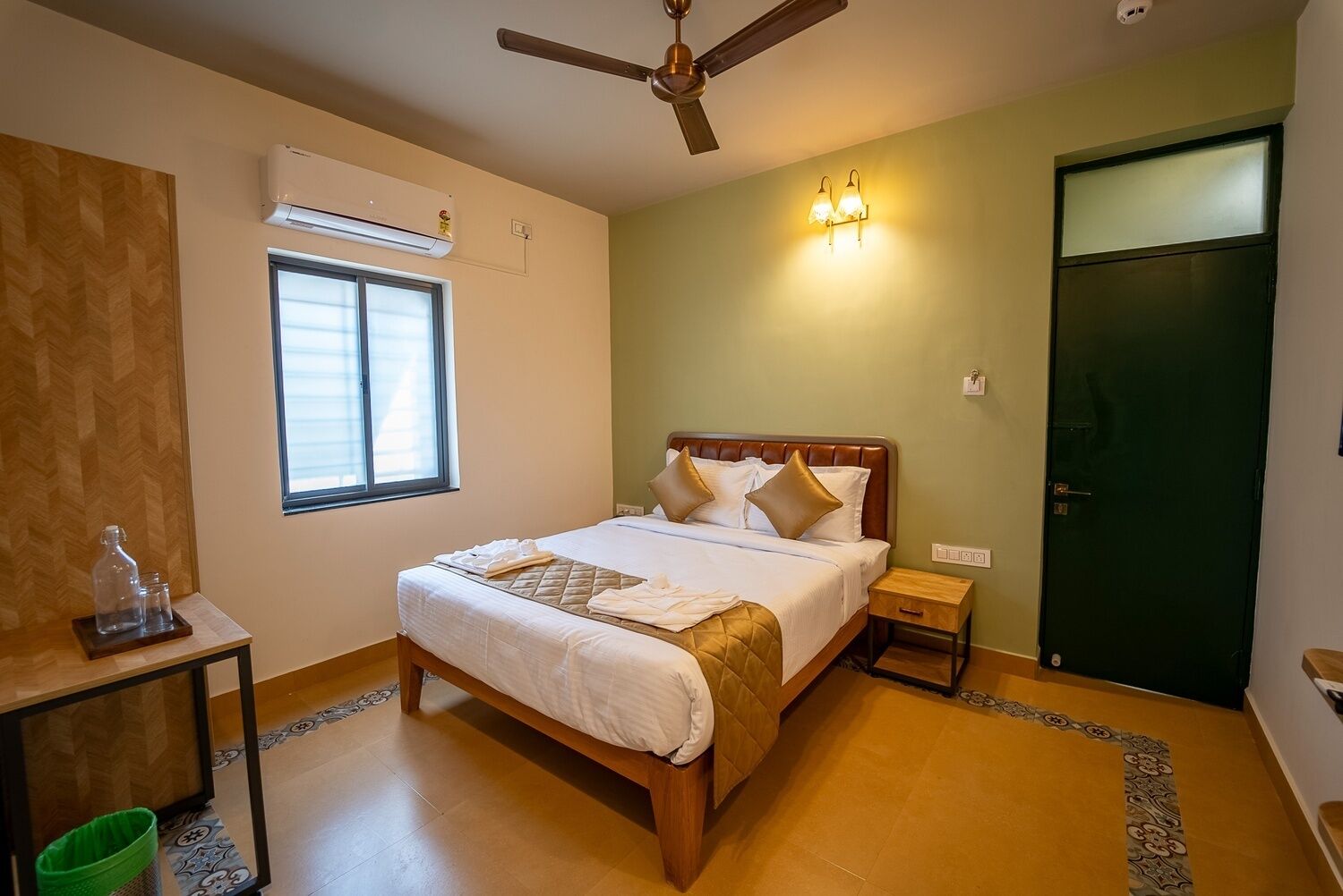 A bedroom with a bed, bedside tables, a window, an air conditioning unit, a ceiling fan, and a door.