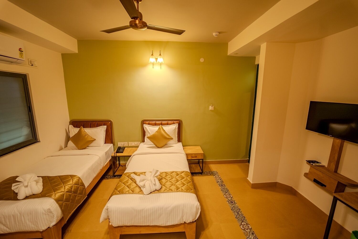 Habitación de hotel con dos camas, televisión, ventilador de techo y una mesita.