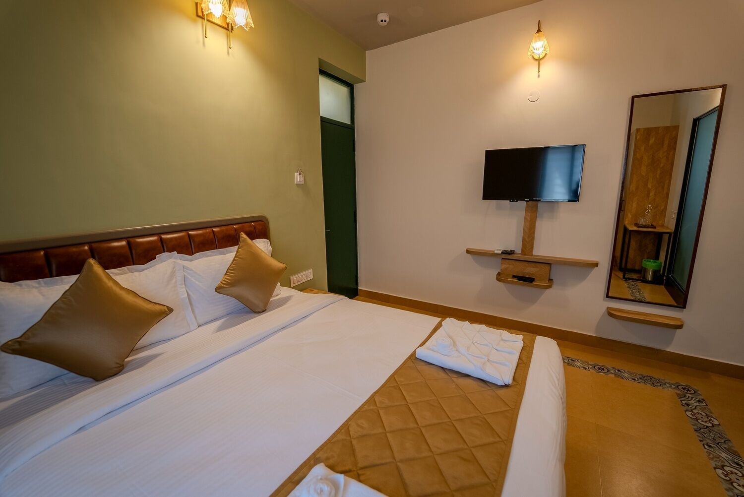 A hotel room with a bed, a TV, a mirror, and a small shelf.