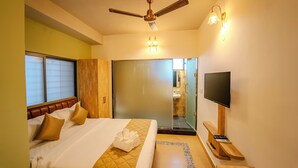 A hotel room with a bed, a ceiling fan, a television, and a bathroom visible through a glass door. - Atithyaa (Bengaluru)