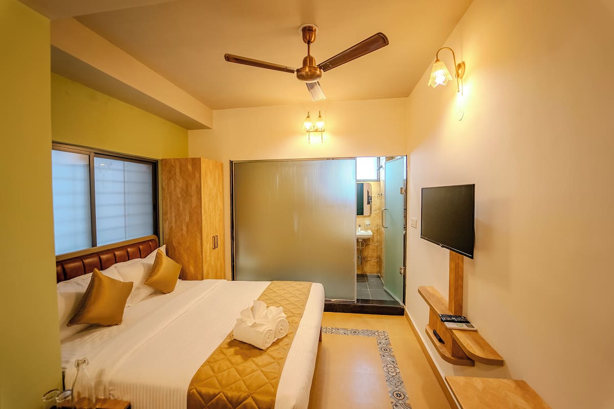 A hotel room with a bed, a ceiling fan, a television, and a bathroom visible through a glass door.