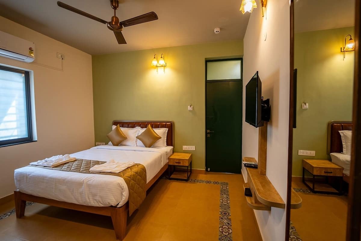 A hotel room with a bed, a ceiling fan, a TV, and a green door.