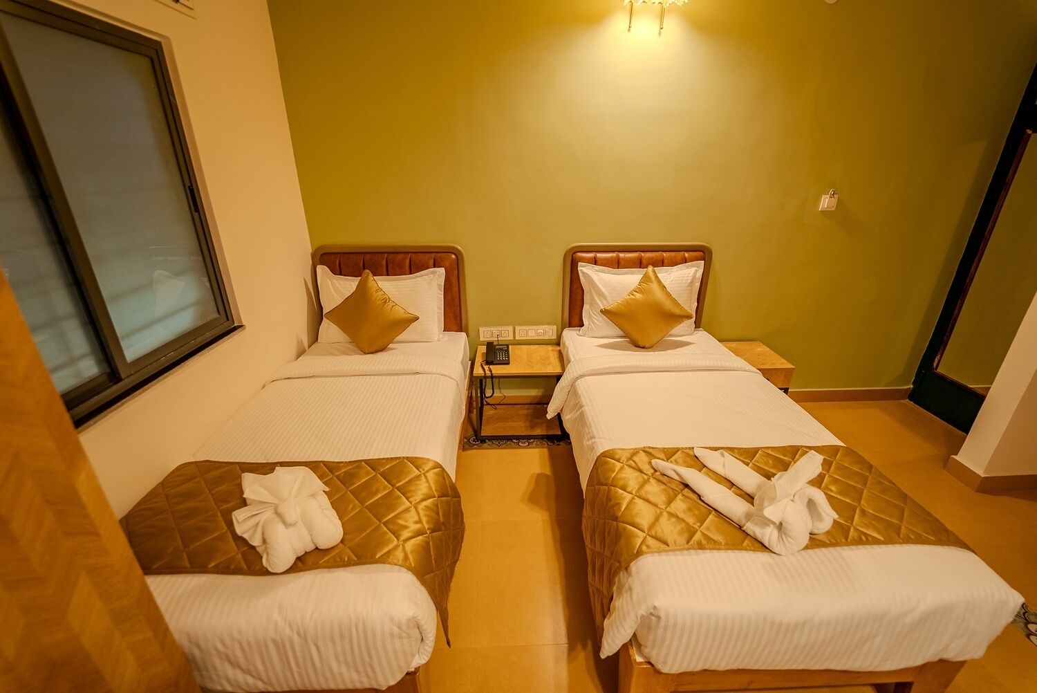 A hotel room with two beds, a window, a bedside table with a phone, and a wall socket.