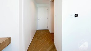 Un corridoio stretto con pavimento in legno, pareti bianche e una porta in fondo.