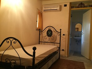 A single bed with a metal frame and a headboard with a decorative mirror. There is a wall-mounted air conditioner above the bed.