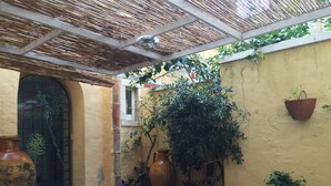 A courtyard with a tiled floor, a large potted plant, a hanging planter, and a door with a decorative design. - La Casa Di Levante, Charming apartment with panoramic terrace. (Milazzo)