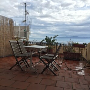 A patio with a table and chairs, a fence, and a view of the sea.