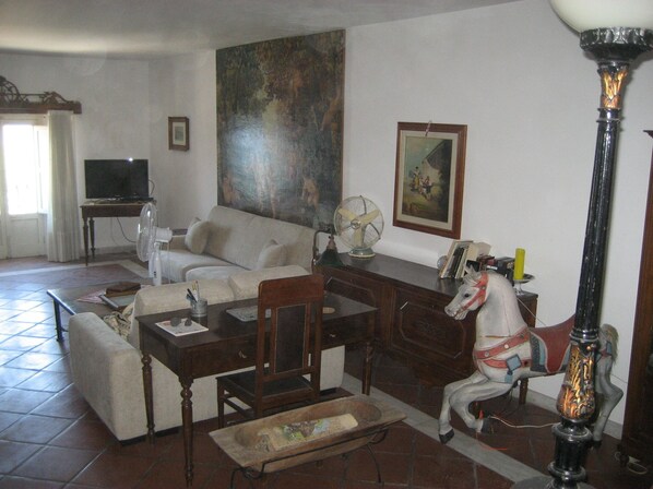 A living room with a sofa, a dining table, a TV, a fan, a horse sculpture, and a painting on the wall.