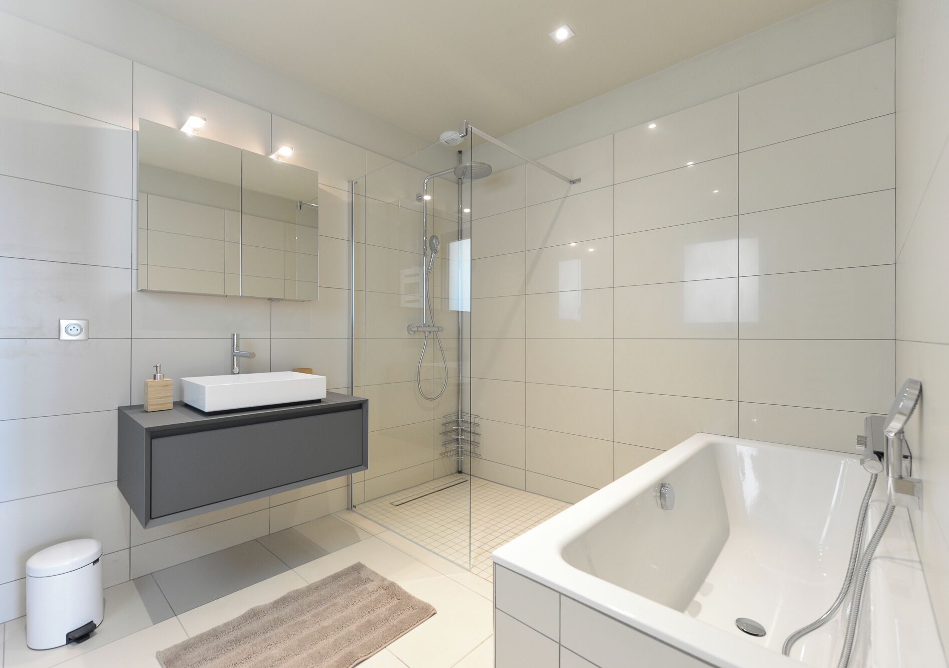 A modern bathroom with a large bathtub, a glass-enclosed shower, a vanity with a sink, and a mirror.