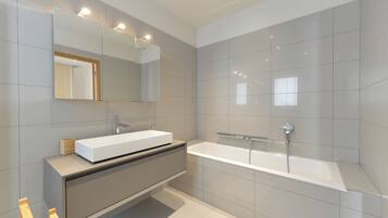 A modern bathroom with a large mirror, a white sink, and a freestanding bathtub.