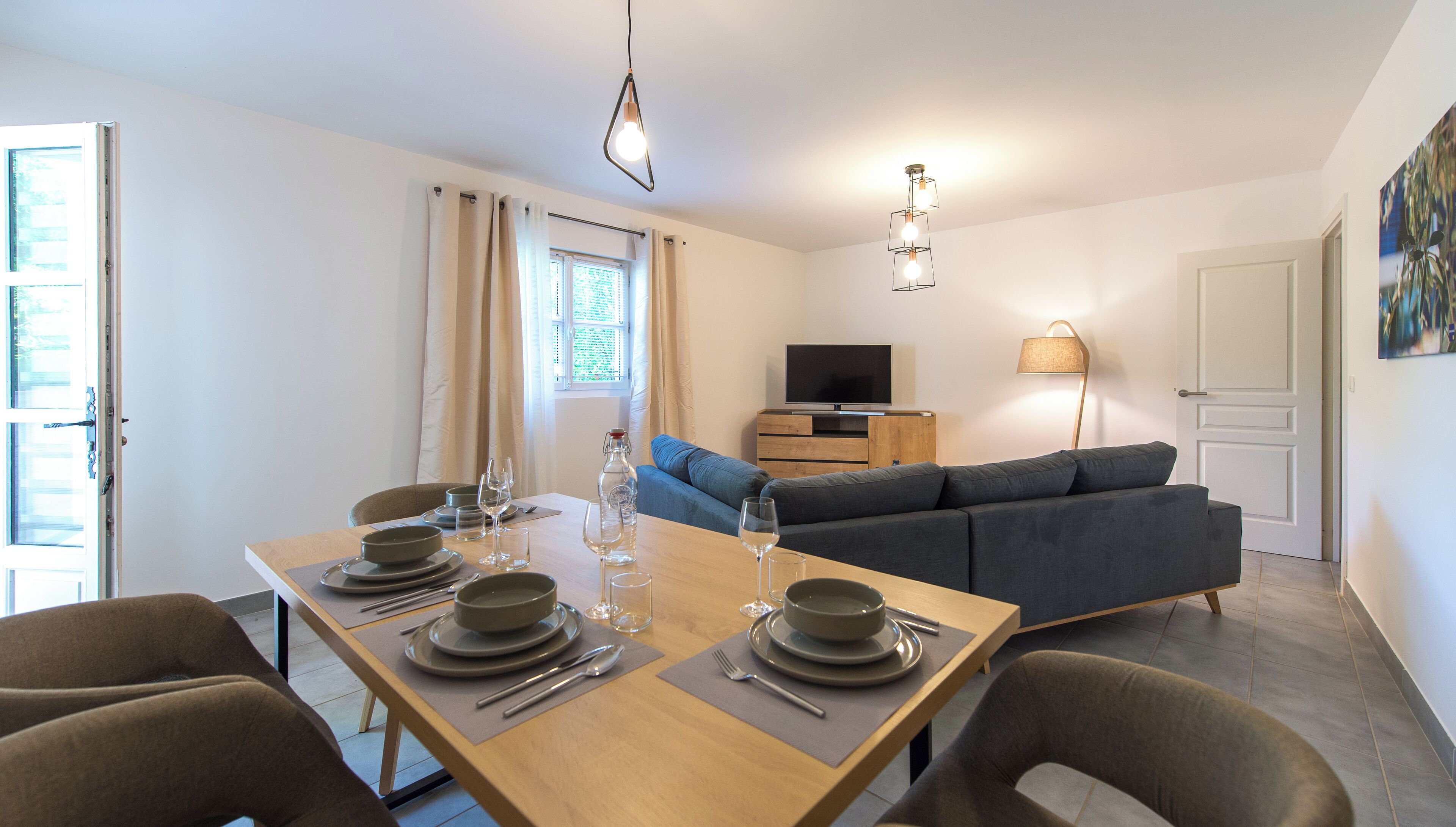 Un coin repas avec une table en bois dressée pour quatre personnes, un canapé, un téléviseur et une lampe.