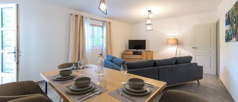 Un coin repas avec une table en bois dressée pour quatre personnes, un canapé, un téléviseur et une lampe.