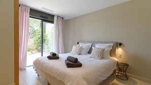 A modern bedroom with a large bed, two pillows, a bedside table, and a view of greenery through the window.