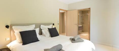 Ein modernes Hotelzimmer mit einem großen Bett, einem Nachttisch und einer großzügigen Dusche.