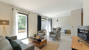 A modern living room with a sofa, armchairs, a coffee table, and a dining area with a table and chairs.