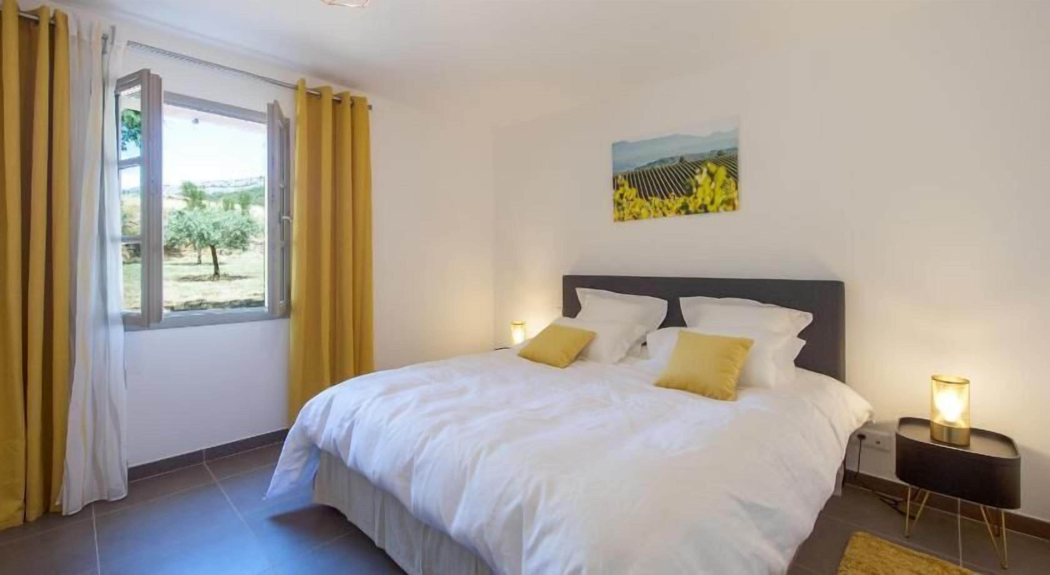 A bedroom with a large bed, two bedside tables, a window with curtains, and a painting on the wall.