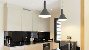 A modern kitchen with a black countertop, white bar stools, and pendant lighting.