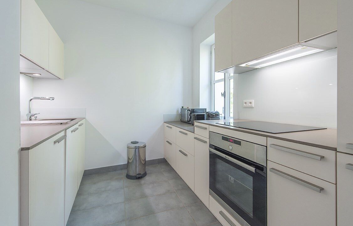 A modern kitchen with white cabinetry, a stainless steel sink, a trash bin, a toaster, and a built-in oven.