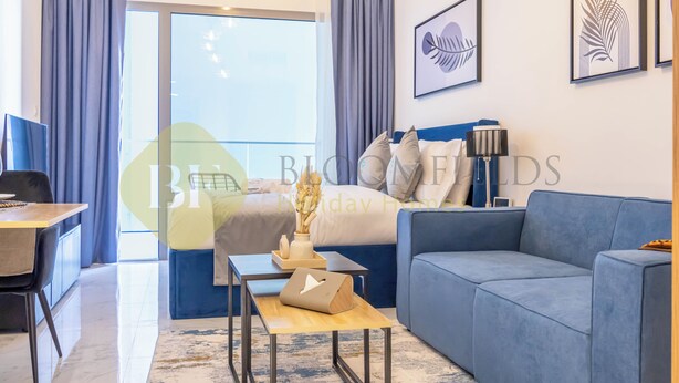 A modern hotel room with a bed, a blue sofa, a small table, and a desk.