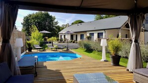 Un espacio al aire libre techado con piscina, sillas de descanso y una pérgola.