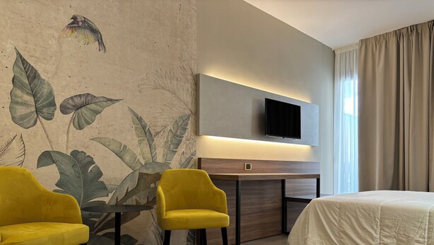 A hotel room with a bed, two yellow armchairs, a small table, a flat-screen TV, and a large window with curtains. - Casa Vacanze Fardella Centrale (Trapani)