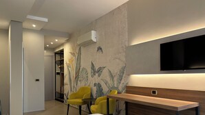 A hotel room with a bed, a desk, two yellow chairs, a TV, and a wall with a tropical plant mural. - Casa Vacanze Fardella Centrale (Trapani)