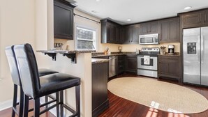 A modern kitchen with dark wood cabinets, stainless steel appliances, and a black leather bar stool. - The Red Door House in Historic Georgetown (Georgetown)