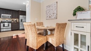 A dining area with a round table and four wicker chairs, a kitchen in the background, and a 'Welcome' sign on the wall. - The Red Door House in Historic Georgetown (Georgetown)