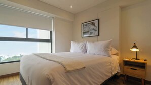 A bedroom with a large bed, a bedside table with a lamp, a framed picture on the wall, and a window with a view. - w* | Pleasant 3BR w/ Balcony in San Isidro (Lima)