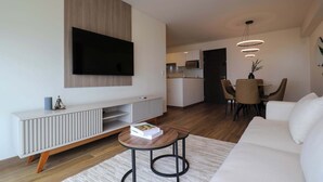 A modern living room with a flat-screen TV, a white sofa, a dining area with chairs, and a kitchen in the background. - w* | Pleasant 3BR w/ Balcony in San Isidro (Lima)