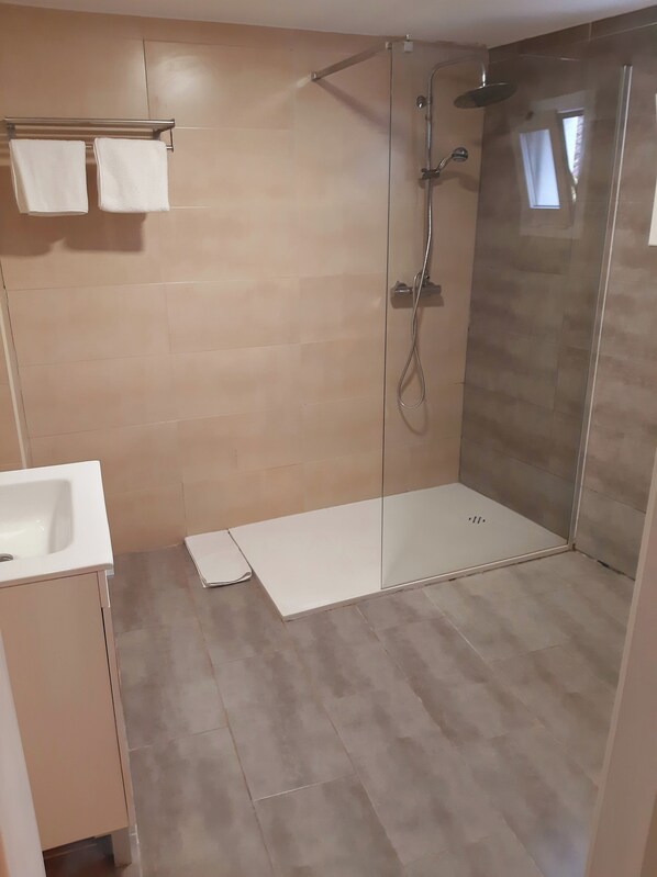 Un baño moderno con ducha de vidrio, lavamanos blanco y paredes con azulejos color beige.