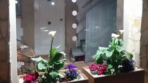 Un bagno con un grande specchio, due vasi di fiori assortiti e un pavimento piastrellato.