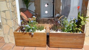Una fioriera in legno con fiori, una sedia in vimini con cuscini e una porta con pannello di vetro.