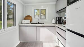 A modern kitchen with white cabinetry, a built-in oven, a coffee maker, and a toaster. - Leos Beach Hideaway, Stylish Tiny Home (Coffs Harbour)